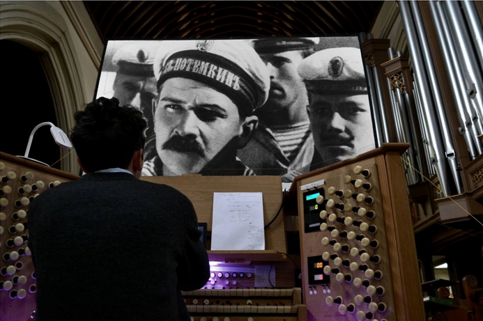 adam dickson at the organ with Potemkin sailors on the screen
